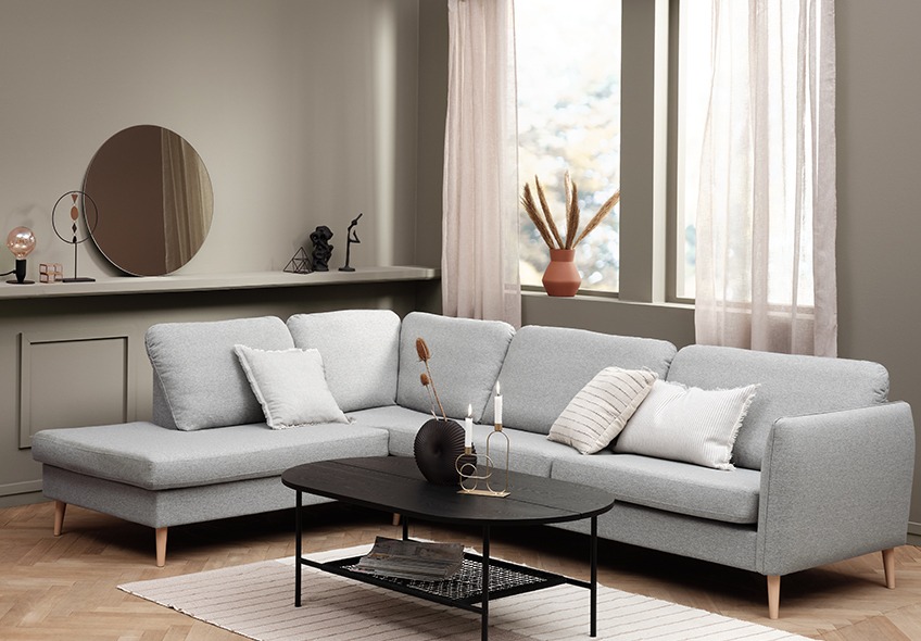 Stue med en stor grå sofa med pufafslutning og et sort sofabord