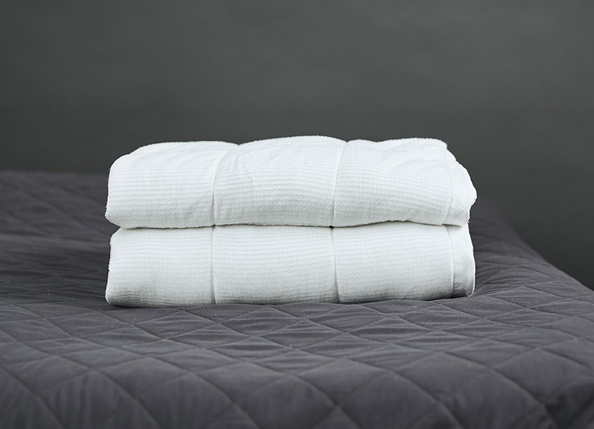 En vægtdyne foldet oven på en seng med en mørkegråt sengetæppe