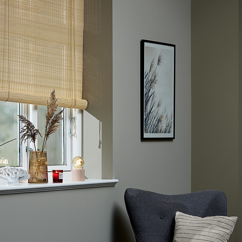 Bambus rullegardin i vinduet med en vase, et duftlys og en batterilampe i vindueskarmen