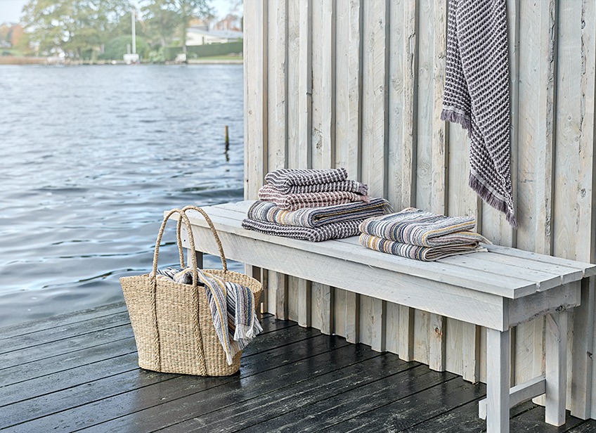 Håndklæder på en bænk og i en taske ved en sø