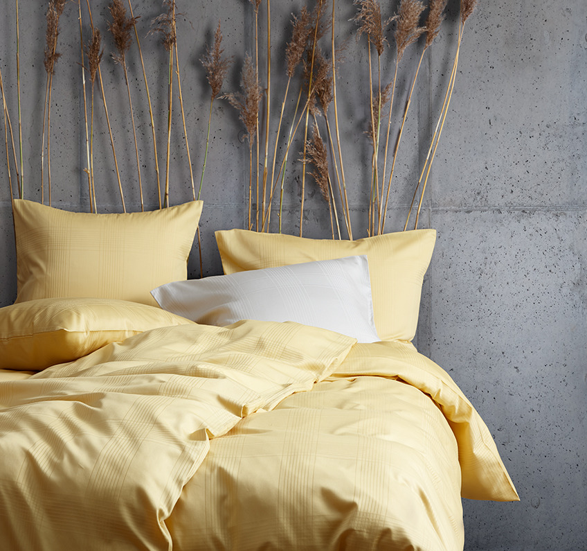 Gult sengetøj af 51% genanvendt polyester og 49% bomuldssatin i et soveværelse dekoreret med tørrede græsser