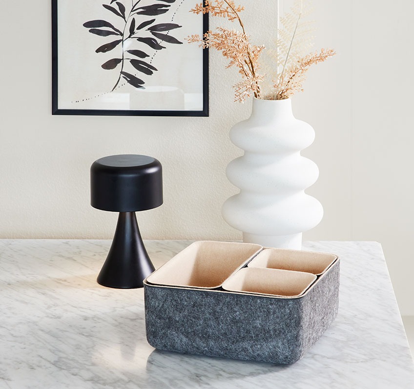 Filtkurv, hvid vase og batterilampe på et bord