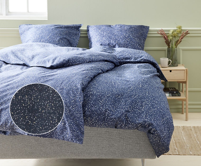 Seng med blåt sengetøj I soveværelse med natbord og bordlampe