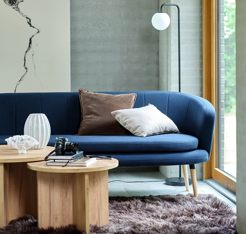 Blå sofa, runde sofaborde, brunt tæppe og gulvlampe
