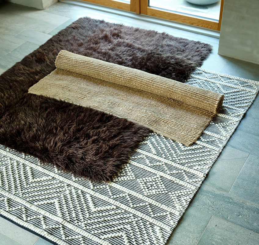 Brunt tæppe, mønstret tæppe og jutetæppe på gulvet
