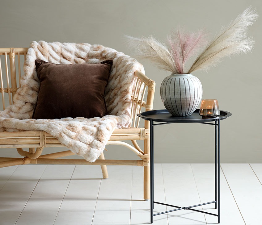 Sofa med plaid i imiteret pels og brun pude. Sort hjørnebord med vase og fyrfadsstage