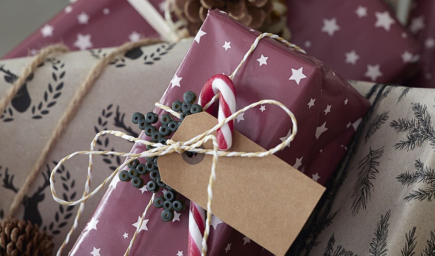 Julegave pakket ind i gavepapir og pyntet med sukkerstok og perleplade