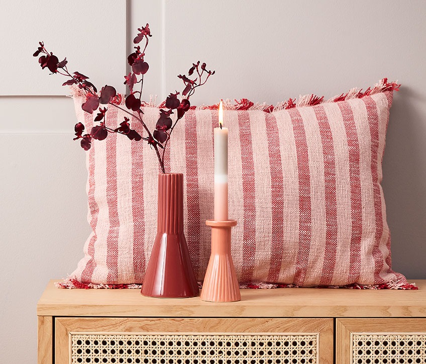 DAGFIOL pude, RAGNAR kunstige blomster, EGMUND vase og THRISTAN lysestage med IGNI lys Stribet pude bag rød vase og lysestage med stribet lys
