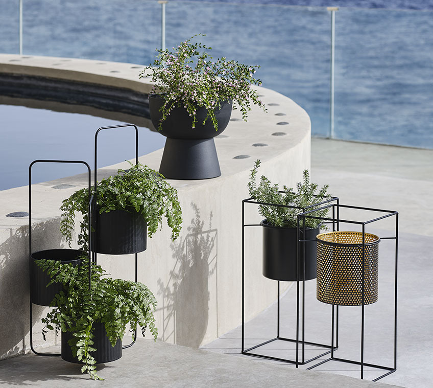 AND blomsterpotteholder med tre potter, sort LOMVI havekrukke og MIDSOMMER havekrukke, der fås i sort eller guldfarvet Havekrukker på ben på en stor altan