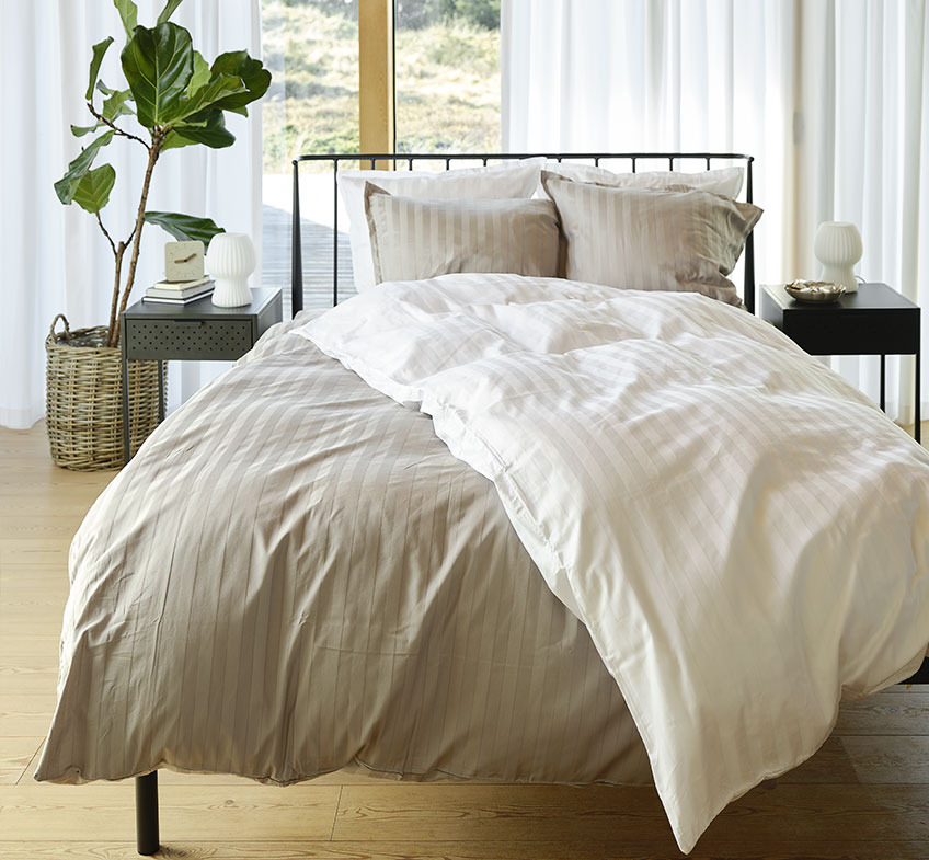 Soveværelse med grå- og hvidstribet sengetøj på sengen og to natborde