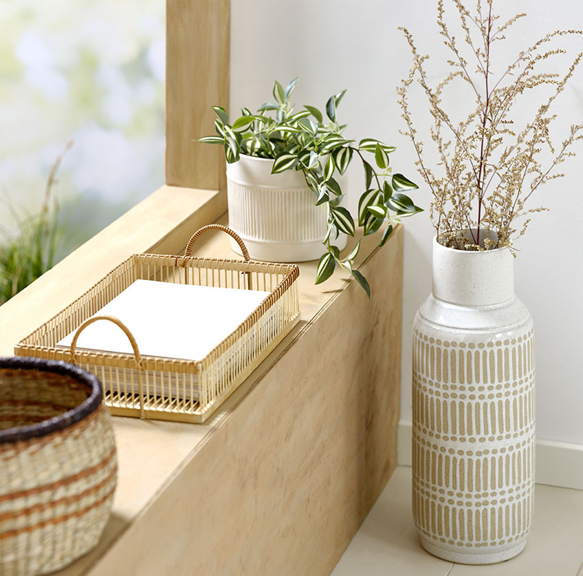 Høj vase ved vindueskarmen med bambusbakke og hvid plantekrukke med kunstig plante