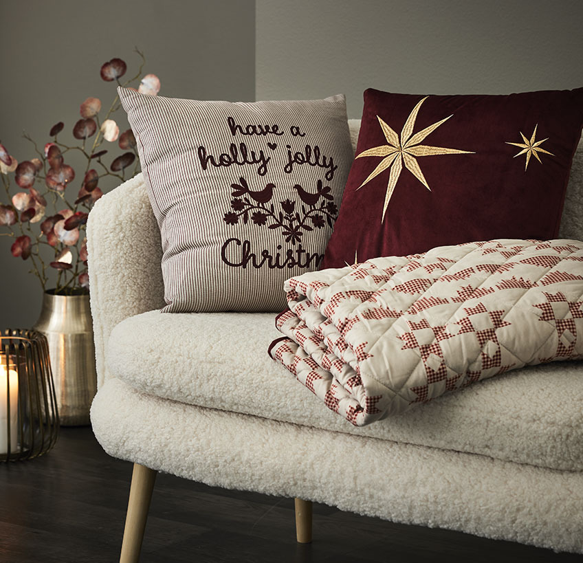 Hynder og quiltet tæppe med julemotiver i hvid sofa