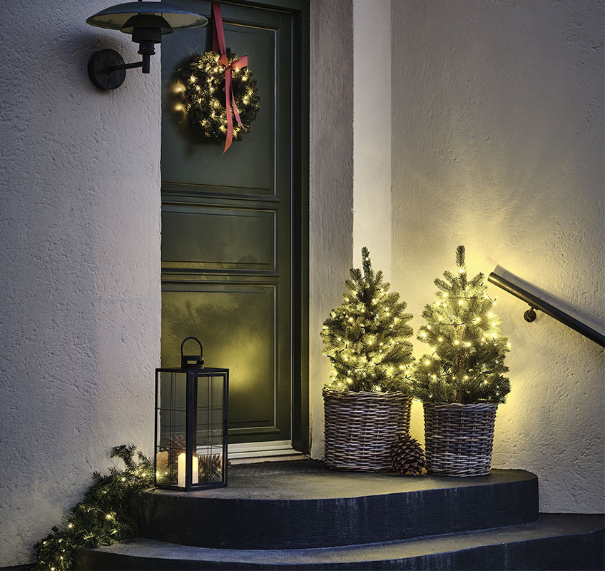 To lys træer foran hoveddør og julekrans med rød sløjfe