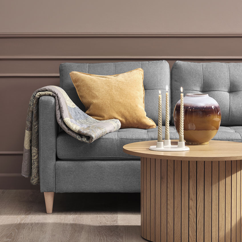Vattæppe og gul pyntepude på grå sofa, sofabord af træ med stearinlys og vase