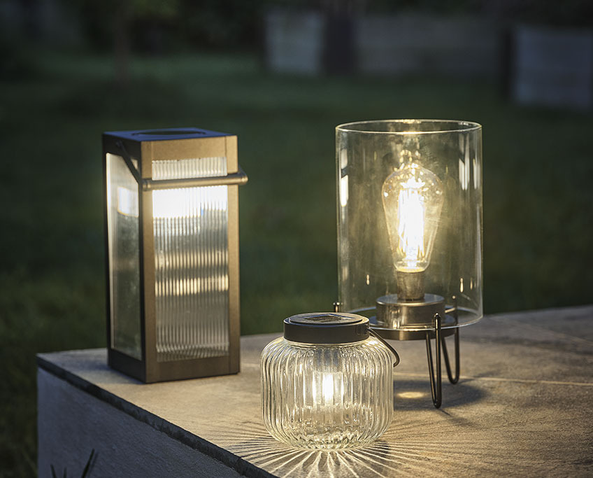 ISFUGL og SVARTSPETT solcellelampe og ALKEKONGE batterilampe Tre havelamper på et bord