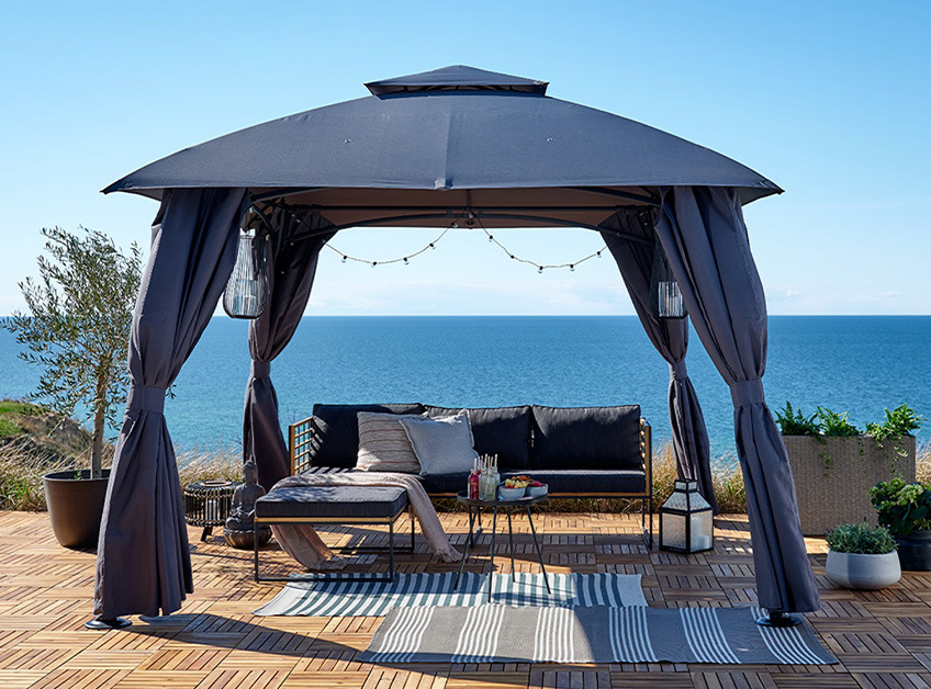 Grå pavillon med loungesæt og lyskæder med udsigt over havet