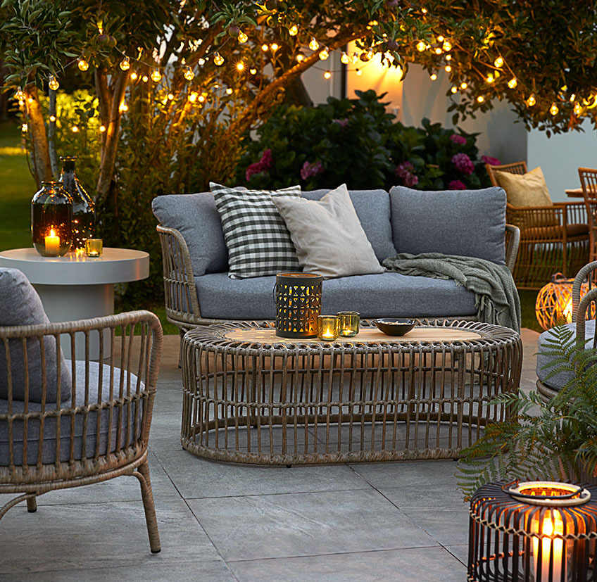 Komfortable loungemøbler på terrasse med havelamper i form af lyskæder, batterilamper og lanterner med stearinlys og fyrfadslys
