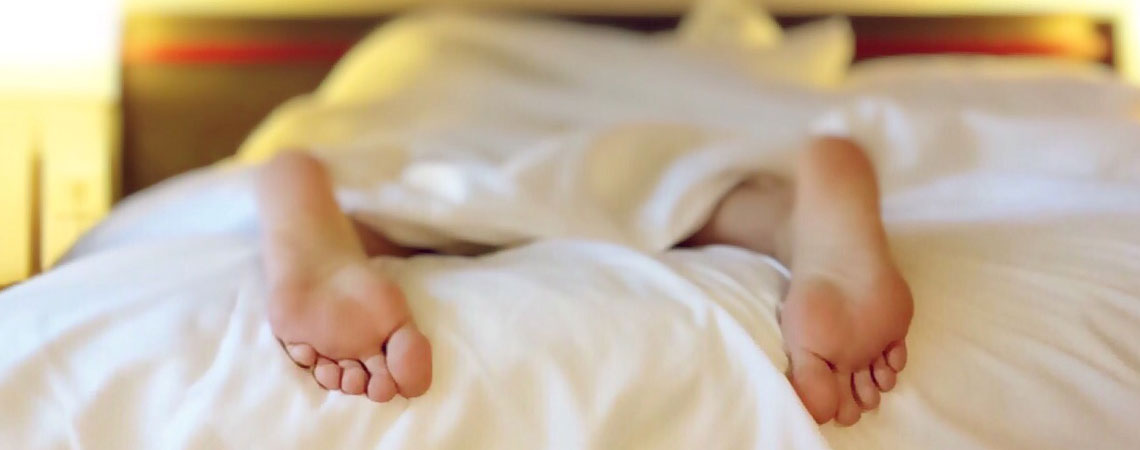 Person der sover i en seng med fødderne stikkende ud under dynen